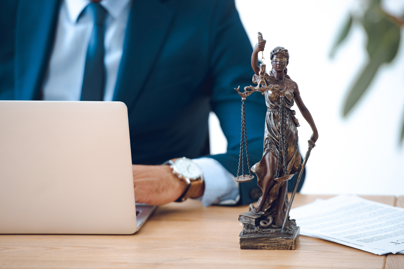 Cropped shot of lawyer using laptop and lady justice statue on table